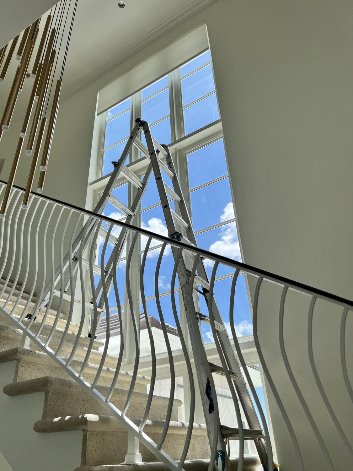Two-story stairwell window with no shade, a ladder standing in front
